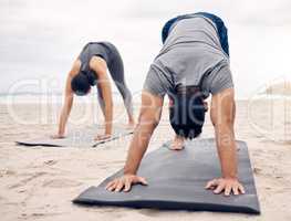 Building strength while stabilising muscles and coordination. Shot of a sporty young couple doing a downward facing dog pose while practising yoga together on the beach.