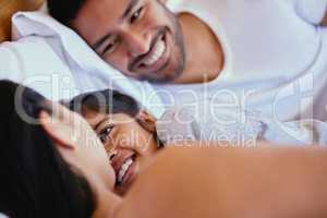 Adorable little girl smiling while lying in bed with her parents. Mixed race family with one child relaxing and bonding in the morning while still lying in bedroom