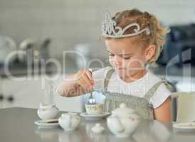 A little girl having a tea party at home. Cute brunette female wearing a tiara while playing with tea set and having cookies at kitchen table.