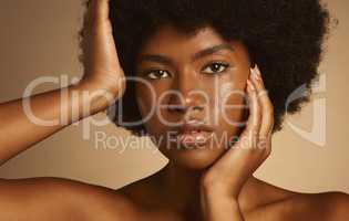 Young African woman with afro hair and glowing radiant skin posing against a brown studio background. One female only wearing natural makeup and looking confident with flawless complexion