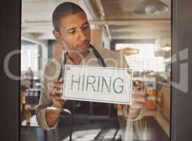 Business owner looking to hire new staff. Young businessman hanging a hiring sign in his shop entrance. Boss working in coffeeshop hiring new employees. Hr employee hanging hiring signage in shop