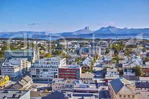 Aerial view of Bodo city in Norway on a sunny day with a blue sky. Scenic modern urban landscape of streets and buildings near a mountain horizon with copy space. Peaceful rural town from above