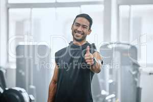 Portrait of smiling trainer alone in gym, showing thumbs up sign and symbol. Asian coach endorsing support after workout in exercise health club. Young happy man in fitness centre for routine training