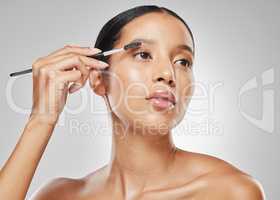 Hey girl, nice brows. Studio shot of an attractive young woman using an spoolie brush to comb her eyebrows against a grey background.