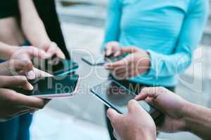 Closeup of diverse group of sporty people using cellphones with blank screens in synchronicity while standing in a circle around each other. Hands of athletes browsing online and searching the internet in a huddle. Downloading and sharing media