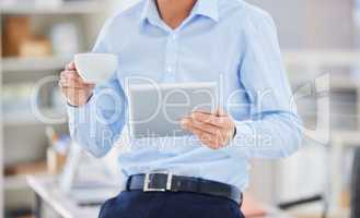 Closeup of on businessman browsing on a digital tablet while drinking coffee from a teacup during a break in an office. Entrepreneur planning online while searching for ideas and inspiration on his wireless and portable smart device