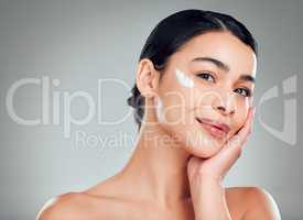 Studio Portrait of a beautiful smiling mixed race woman applying cream to her face. Hispanic model with glowing skin grey copyspace background