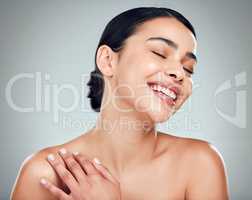 A beautiful young mixed race woman with glowing skin posing against grey copyspace background. Hispanic woman with natural looking eyelash extensions smiling while feeling her smooth skin in a studio