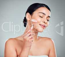 One beautiful mixed race woman using a rose quartz derma roller during a selfcare grooming routine. Young hispanic woman using anti ageing tool against grey copyspace background