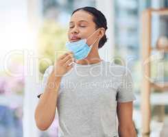 Young mixed race woman taking off her covid face mask and breathing fresh air inside a room. Hispanic enjoying clean oxygen after wearing disposable mask. Healthy and protected from virus pandemic
