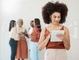 Portrait of a young happy mixed race businesswoman with a curly afro holding and using a digital tablet in an office at work. Hispanic businessperson smiling while using social media on a digital tablet