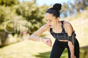 One active young mixed race woman checking digital smartwatch while training outdoors. Hispanic athlete wearing fitness tracker with stopwatch to monitor progress, heart rate and calories burned during exercise