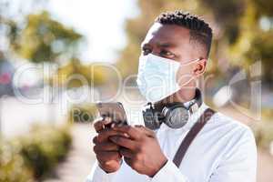 Unrecognizable black man wearing a mask to protect himself from the corona virus pandemic while wearing earphones and texting on a cellphone. Businessman walking to a an interview using gps on a phone