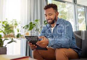 Handsome bachelor reading on his digital tablet. Happy bachelor enjoying his day at home relaxing. Always connected to the online world with his wireless tablet. Young man resting on his couch