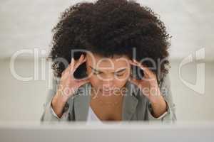 Young mixed race businesswoman suffering from a headache while working on a desktop computer in an office at work. One stressed hispanic businessperson with a curly afro suffering from anxiety and looking upset from above