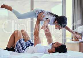 Dad lifting daughter in the air while lying on bed. Young father playing with adorable little daughter and enjoying a family weekend together. Loving and caring dad practising acroyoga with child