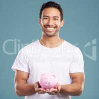 Handsome young mixed race man holding his pink piggybank while standing in studio isolated against a blue background. Hispanic male showing savings, finance, investment, wealth management and banking