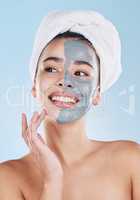 Beautiful young mixed race woman applying a face mask peel isolated in studio against a blue background. Attractive woman with a towel on her head after a shower. Her skincare regime keeps her fresh