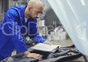 Going through his checks. a handsome young male mechanic working on the engine of a car during a service.