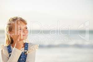 One adorable little girl thinking of ideas while standing on a beach outdoors. A cute young kid looking thoughtful while outside with the sea in the background. The mind and imagination on a child