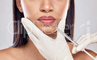 Its only a pinch. Shot of a woman having her lips injected with filler against a studio background.