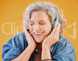 One happy mature caucasian woman wearing headphones and listening to music while dancing against a yellow background in the studio. Smiling white woman feeling free while expressing through dance