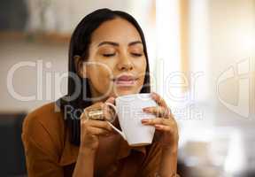 Young happy beautiful mixed race woman enjoying a cup of coffee alone at home. Hispanic female in her 20s smiling while drinking a cup of tea in the kitchen at home