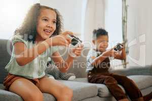 Two happy mixed race siblings relaxing on the lounge sofa together while playing fun video games. Children only competing while playing games at home on the weekend
