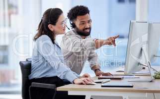 Young caucasian call centre telemarketing agent discussing plans with mixed race colleague on a computer in an office. Two consultants troubleshooting solution for customer service and sales support