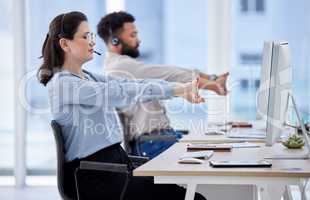 Young caucasian call centre telemarketing agent stretching her arms while working alongside a colleague in an office. Two consultants taking a break to get ready to operate helpdesk for customer service and sales support