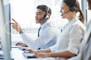 Probably the most competent call centre staff youll ever dealt with. Shot of a man pointing at his computer while wearing a headset in a call center.