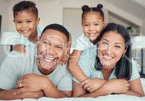 Portrait of a cheerful family lying together on bed. Little boy and girl lying on their parents laughing and having fun. Mixed race couple bonding with their son and daughter. Hispanic siblings enjoying free time with their mother and father