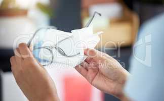 An unrecognizable woman cleaning her glasses in her apartment. One unknown woman using a tissue to remove dust from her spectacles