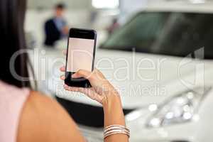 Im showing off my new ride on social media. a woman taking picture on her cellphone at a car dealership.