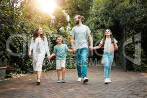 Happy young caucasian family of four holding hands and going for a walk in the neighbourhood. Carefree parents with their two children leaving their residence and going for a sunny stroll