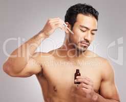Handsome young mixed race man posing shirtless in studio isolated against a grey background. Hispanic male applying antiaging serum to his face using a dropper. All part of his skincare regime