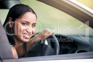 Cheerful mixed race woman driving her new car. Smiling young woman looking out her car window in the drivers seat and going for a drive. Passing out for drivers license or test drive. Car insurance