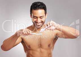 Closeup young mixed race man shirtless in studio isolated against a grey background. Hispanic male brushing his teeth. Taking caring of mouth and oral hygiene to promote dental health and healthy gums