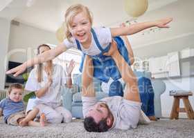 Portrait of a happy caucasian family of four having fun while being playful on the lounge floor carpet at home. Young positive couple with two smiling chidren playing a game at in a bright lounge