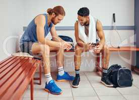 Two players bonding in their gym locker room. Two professional athletes using their cellphones together. Professional squash players talking and using their smartphones to text in the locker room