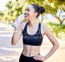 One fit young mixed race woman taking a rest break to drink water from bottle while exercising outdoors. Happy female athlete quenching thirst and cooling down after running and training workout