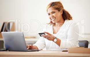 Mixed race happy businesswoman using a credit card and working on a laptop to shop online at work. Hispanic woman paying for a purchase. Female making payment using a laptop and bank card