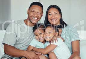 Portrait of a happy young mixed race family with two children wearing pyjamas and sitting at home together. Loving little sister and brother embracing each other while spending time with their parents on the weekend