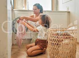 Young hispanic mother and her daughter sorting dirty laundry in the washing machine at home. Adorable little girl and her mother doing chores together at home