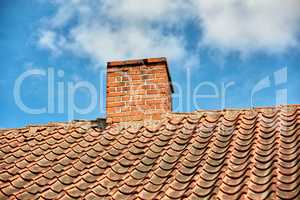 Red brick chimney designed on the roof of residential house or building outside against a cloudy sky background with copyspace. Air vent construction for the release of smoke and heat from fireplace