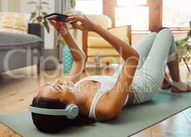 Downloading a few cool songs for her next session. a sporty young woman wearing headphones and using a cellphone while exercising at home.