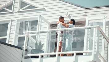 Loving young mixed race couple in pyjamas sharing romantic moment while dancing on the balcony of their new home or while on holiday enjoying their honeymoon