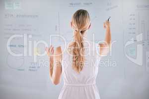 One caucasian businesswoman from behind brainstorming plans with graphs, stats and analytics on a whiteboard. One female only thinking of ideas and strategies while doing market research for startup