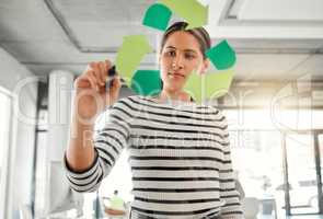 Young focused mixed race businesswoman drawing a recycle symbol on a glass window in an office at work. One hispanic businessperson drawing a sign for awareness to recycling