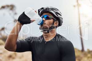 Thirsty cyclist taking a break and drinking water from a bottle. Fit young man wearing glasses and a helmet while drinking water and standing outside. Athletic man cycling in nature environment